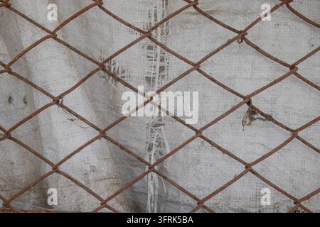 Rostige Metall-Drahtgeflecht-Zaunstruktur im Nahaufnahme mit weißem Polypropylen-Stoffhintergrund. Industrielles Sicherheitsnetz-Muster als Hintergrund für Bau Stockfoto