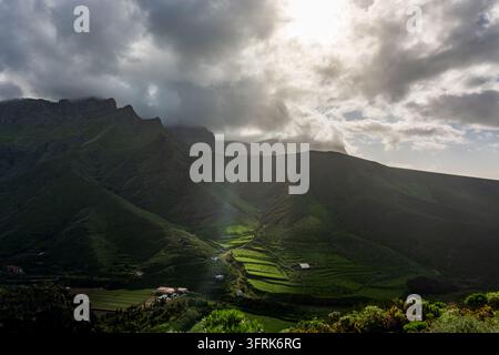 Sonnenlicht bricht durch dramatische Wolken über den Bergen des Agaete-Tals und erhellt grüne landwirtschaftliche Terrassen und Farmen darunter, Gran Canaria Stockfoto