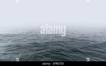 Ein ruhiger Ozean mit sanften Wellen erstreckt sich bis zu einem nebligen Horizont. Stockfoto