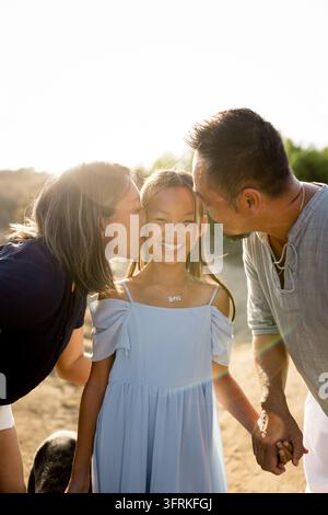 Liebevolle Eltern küssen die Wangen ihrer lächelnden Tochter Stockfoto