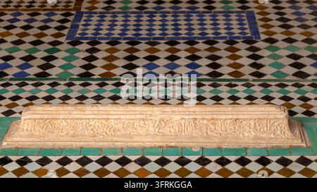 Aufwendig geschnitzter Marmorgrabstein mit arabischer Kalligrafie vor traditioneller geometrischer Zellige-Fliesenverkleidung in den Saadier-Gräbern in Marokko. Stockfoto
