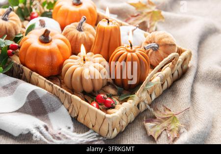 Gemütliche Herbstszene mit dekorativen Kürbiskerzen, Blättern und Hagebutten in einem gewebten Tablett Stockfoto