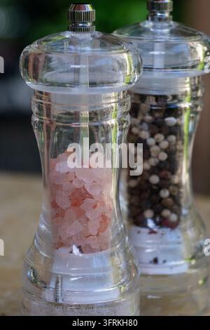 zwei transparente Glas-Mühler gefüllt mit rosa Himalaya-Salz und gemischten Pfefferkörnern, die auf einer Küchenoberfläche stehen. Stockfoto