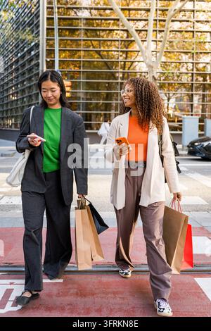 junge Frauen gehen auf der Stadtstraße während des Einkaufs und halten Tüten, Einkäufer in der Wintersaison, Paar in ihren 30ern Stockfoto
