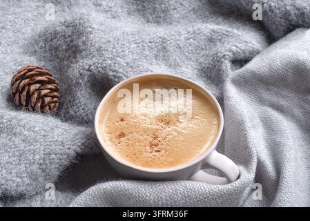 Tasse Kaffee auf grauem weichem Stricktextil als Hintergrund. Morgenentspannung, gemütliches Winter- und Home-Comfort-Konzept im Nahaufnahme. Stockfoto