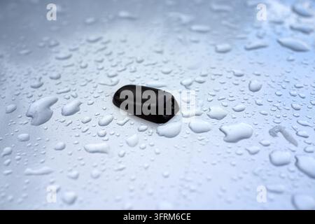 Schwarzes Smartphone auf nassem Glas mit Wassertropfen und weichem blauem Unschärfehintergrund. Stockfoto