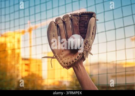 Baseballhandschuh fing den Ball auf dem Feld. Im Hintergrund sind Stadionnetze und verschwommene blaue und gelbe Herbstfarben der Natur zu sehen. Stockfoto