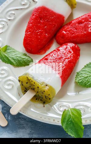 Teller mit hausgemachten Eis am Stiel mit Kiwi, Joghurt und Erdbeeren auf einem grauen Betonhintergrund Stockfoto