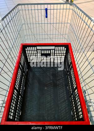 Leerer Einkaufswagen mit roter Kunststoffkiste im Inneren, bereit für Lebensmitteleinkäufe im Supermarkt Stockfoto