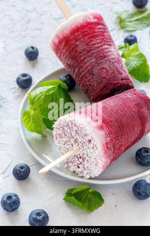 Hausgemachte vegane Beeren-Eis am Stiel mit Kokosmilch, frischen Blaubeeren und grüner Minze auf einem weißen Betonstisch Stockfoto