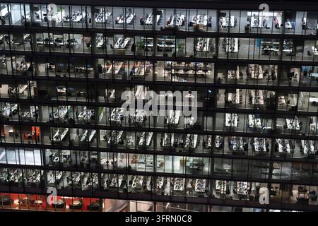 ANGESTELLTE ARBEITEN LATE IN EINEM GLASBÜROGEÄUDE, CITY OF LONDON, ARCHIVREPORTAGE, LONDON, ENGLAND, 2019: Von außen bei Nacht gesehen zeigt die beleuchtete Glasfassade eines großen, modernen Bürogebäudes ein rasterartiges Muster von Stockwerken, in denen viele Menschen noch arbeiten. INFO: Die City of London, auch bekannt als das Quadratmeil, ist Londons historischer Kern und führender globaler Finanzdistrikt. Unter ihrer eigenen einzigartigen, alten kommunalen Regierung betriebend, vermischt sie ultramoderne Wolkenkratzer mit alten ikonischen Wahrzeichen. Stockfoto