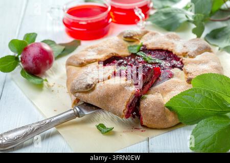 Hausgemachte Galette mit roter Pflaumenfüllung auf einem Blatt Backpapier auf einem weißen Holztisch, selektive Schärfe Stockfoto