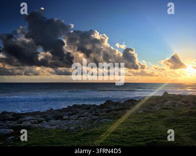 Sonnenuntergang über dem Mittelmeer in der Nähe von Paphos, Zypern, wobei die Sonne lebendiges Licht über die Szene wirft. Der Himmel zeigt dramatische Wolkenformationen Stockfoto