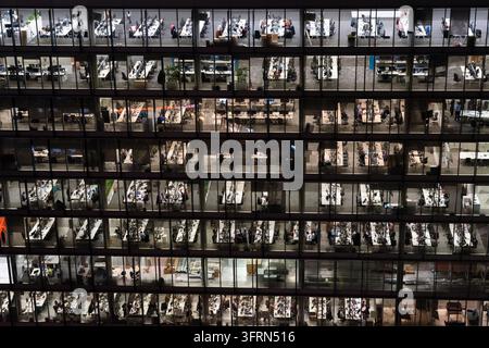 BÜROANGESTELLTE IN EINEM GLASGEBÄUDE IN DER NACHT, CITY OF LONDON, ARCHIV-REPORTAGE, LONDON, ENGLAND, 2019: Von außen bei Nacht gesehen sind mehrere Stockwerke eines Glasfrontgebäudes beleuchtet, die Silhouetten von Menschen zeigen, die spät an ihren Schreibtischen arbeiten. INFO: Die City of London, auch bekannt als das Quadratmeil, ist Londons historischer Kern und führender globaler Finanzdistrikt. Unter ihrer eigenen einzigartigen, alten kommunalen Regierung betriebend, vermischt sie ultramoderne Wolkenkratzer mit alten ikonischen Wahrzeichen. Stockfoto