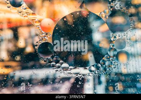 Farbenfroher abstrakter Makroaufnahmen von Öltropfen, die im Wasser schweben, orange und türkisfarbene Lichtreflexionen in flüssigen Blasenstrukturen, kreative Wissenschafts-Flüssigkeitskunst Stockfoto
