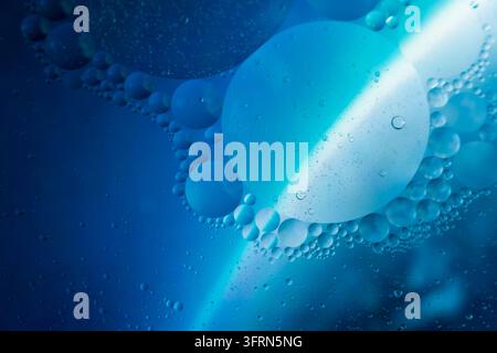 Abstrakte blaue Öltropfen, die in Wasser schweben, Makro-Hintergrund, lebendige flüssige Blasenstruktur mit heller Lichtbrechung, wissenschaftliche Flüssigkeit Stockfoto