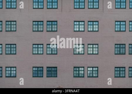 Wiederholte blaue gerahmte Fenster an einer hellen Ziegelgebäudefassade, die ein klares geometrisches urbanes Muster mit leerem Kopierraum erzeugen Stockfoto