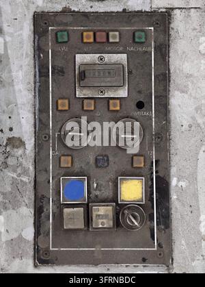 Nahaufnahme einer verwitterten Industrie-Steuerkonsole mit abgenutzten Tasten, Drehschaltern und verblassten Anzeigen auf schmutziger Metalloberfläche, rechteckige Anordnung eingerahmt von weißem Stockfoto
