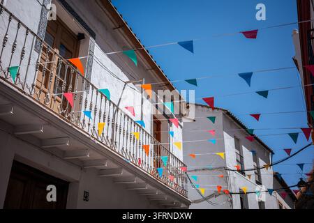 Bunte dreieckige Wimpel hängen über weiß getünchten traditionellen Gebäuden und schmiedeeisernen Balkonen auf einer sonnigen Straße in Setenil de las Bodegas, Anda Stockfoto
