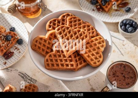Herzförmige belgische Waffeln auf einer Keramikplatte mit Kaffee zum morgendlichen Frühstück. Valentinstag Stockfoto