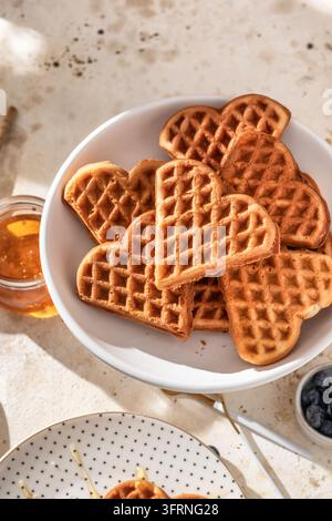 Herzförmige belgische Waffeln auf einer Keramikplatte mit Kaffee zum morgendlichen Frühstück. Valentinstag Stockfoto