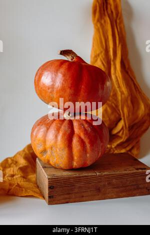 Nahaufnahme von orangefarbenen Kürbissen, die auf einer rustikalen Holzkiste neben warmem goldenem Stoff angeordnet sind. Saisonale Stillleben mit natürlicher Textur, weichem Licht und Kopie Stockfoto