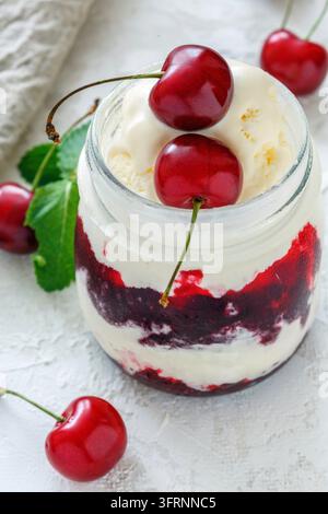 Gläscher mit Eiscreme und süßer Kirsche auf weißem Betonhintergrund Stockfoto