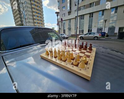 Das Schachbrett liegt auf einem Auto. Das Auto steht auf einer Straße. Es stehen mehrere Autos auf der Straße in der Nähe einer Wohnanlage mit Eigentumswohnungen Stockfoto