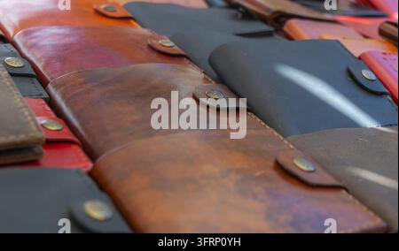 Nahaufnahme von handgefertigten Ledergeldbörsen und -hüllen in Braun-, Schwarz- und Rottönen, die genähte Kanten, Metallverschlüsse und natürliche Ledertextur zeigen Stockfoto