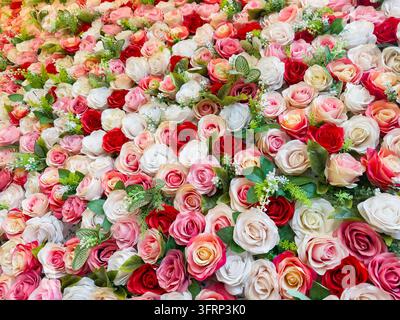 Rosa, weiß und rote künstliche Rosen als Wandhintergrund in einem Restaurant Stockfoto