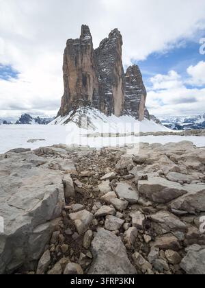 Schnee bedeckt die Berge der Drei Zinnen in den Dolomiten in Italien. Felsen säumen den Pfad, der zu hohen Berggipfeln unter einem Himmel mit Wolken führt. Stockfoto