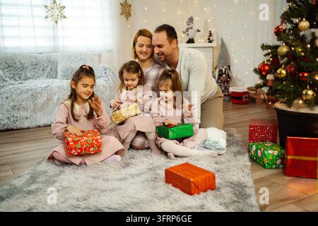 Familie öffnet Weihnachtsgeschenke mit Töchtern an einem festlichen Morgen Stockfoto