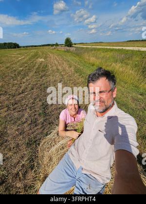 Ein Mann und eine Frau sitzen auf einem Heuballen. Der Mann macht ein Foto von der Frau in der Region Kostroma Stockfoto