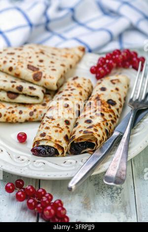 Teller mit traditionellen norwegischen Pfannkuchen, gefüllt mit Beerenmarmelade und Roter Johannisbeere, auf einem alten Holztisch, selektiver Fokus Stockfoto