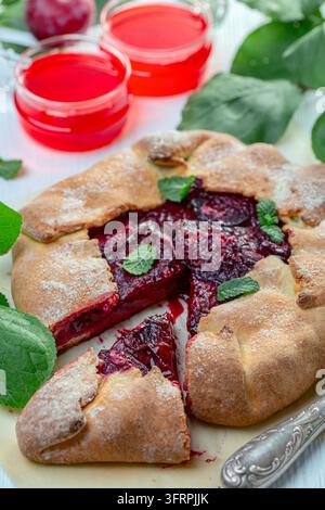 Hausgemachte Galette mit roter Pflaumenfüllung auf einem Blatt Backpapier auf einem weißen Holztisch, selektive Schärfe Stockfoto