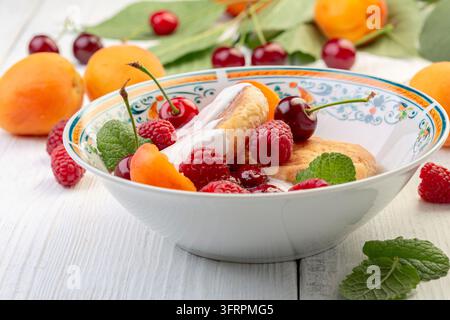Hausgemachte Hüttenkäse-Fritters, Hüttenkäse-Pfannkuchen mit Himbeeren, Kirschen, Aprikosen und Sahnesauce auf einem weißen Teller, selektiver Fokus Stockfoto