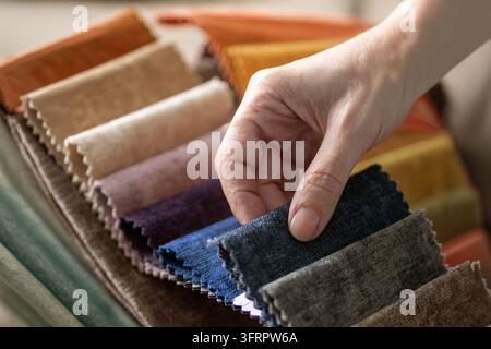 Eine Hand greift nach einem dunklen Farbmuster unter vielen in einem Chenille-Stoffmusterbuch mit rosa geschnittenen Rändern, in Orange, Ocker, Beige, Lila, Pflaume, Blau und Braun. Auswahl Stockfoto