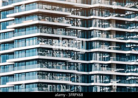 Moderner Hochhaus-Wohngebäude zeigt eine geometrische Fassade mit zahlreichen Glasfenstern und Balkonen, die den Himmel reflektieren Stockfoto