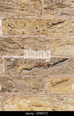 Eine detaillierte Nahaufnahme einer rauen, verwitterten Ziegelwandoberfläche, die deutliche Texturvariationen, Risse und hellfarbige Mörtelnahtverbindungen zeigt, in einer Stockfoto