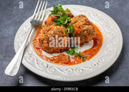 Hausgemachte Fleischbällchen mit Tomatensauce und Sauerrahm auf einem Teller vor einem dunklen strukturierten Hintergrund Stockfoto