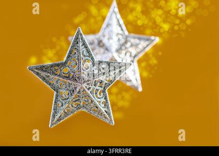 Silberne Weihnachtssterne mit goldenem Hintergrund aus verschwommenen Lichtern. Neujahr- oder Weihnachtskonzept mit Kopierraum Stockfoto