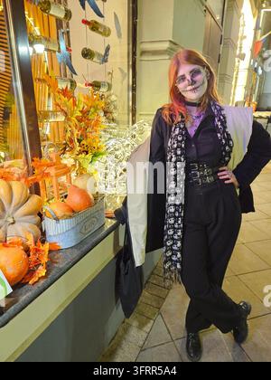 Frau in einem schwarzen Kleid und einem schwarzen Schal steht vor einem Fenster mit einem Kürbis und einer Kürbislaterne Stockfoto