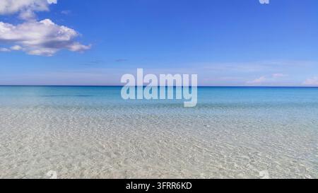 Weite ruhige Meereslandschaft, die ruhiges flaches türkisblaues Wasser über einem Kiesstrand zeigt, der unter einem klaren blauen Himmel auf den fernen Horizont trifft Stockfoto