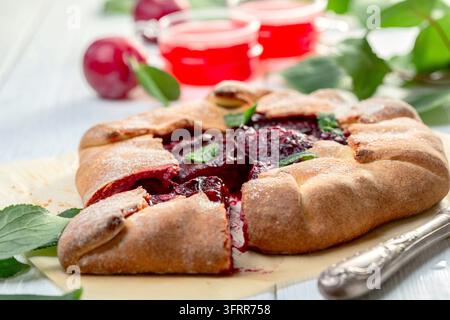 Hausgemachte Galette mit roter Pflaumenfüllung auf einem Blatt Backpapier auf einem weißen Holztisch, selektive Schärfe Stockfoto