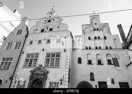 DIE DREI BRÜDER IN SCHWARZ WEISS, RIGA-REISEBERICHT, RIGA, LETTLAND: Eine scharfe Schwarz-Weiß-Aufnahme aus niedriger Perspektive fängt die historischen Fassaden der berühmten Drei-Brüder-Gebäude in Riga ein. INFO: Riga, die Hauptstadt Lettlands, ist die größte Stadt der baltischen Staaten. Mit mittelalterlicher Geschichte und kosmopolitischem Charme vereint, ist sie weltberühmt für ihre atemberaubende, vom UNESCO-Weltkulturerbe gelistete Jugendstilarchitektur und eine wunderschön erhaltene Kopfsteinpflaster-Altstadt. Stockfoto