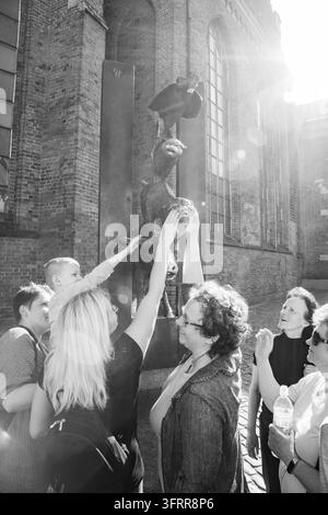 BREMEN STADTMUSIKANTEN-DENKMAL, MENSCHEN BERÜHREN EIN DENKMAL IN SCHWARZWEISS, RIGA REISEBERICHT, RIGA, LETTLAND: In einer Schwarz-Weiß-Aufnahme bei starkem Sonnenlicht streckt eine Gruppe von Menschen, darunter ein kleines Kind, gemeinsam die Hände aus, um eine Skulptur zu berühren. INFO: Riga, die Hauptstadt Lettlands, ist die größte Stadt der baltischen Staaten. Mit einer Mischung aus mittelalterlicher Geschichte und kosmopolitischem Charme ist sie weltweit bekannt für ihre atemberaubende, von der UNESCO gelistete Jugendstilarchitektur und eine wunderschön erhaltene Kopfsteinpflaster-Altstadt. Stockfoto