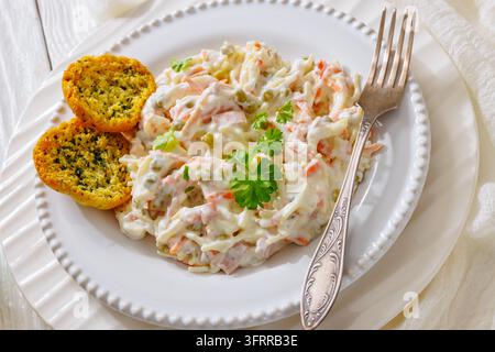 Spiralensalat gemischt mit Karotten, grünen Erbsen und reichhaltigem Mayodressing, serviert neben knusprigem geröstetem Knoblauchbrot auf weißem Keramikteller mit für Stockfoto