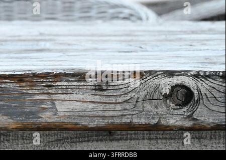 Fotografie, die eine alte, verwitterte Holzoberfläche zeigt, die einen deutlichen Astknoten, natürliche Holzmaserung und Spuren von weißer Farbe aufweist Stockfoto