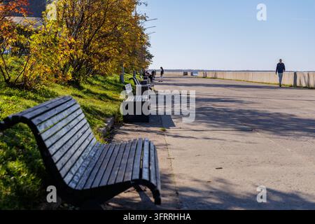 Scenische Ansicht eines Küsten-Steinpfades mit eleganten Holzbankens und goldenen Herbstbäumen in Nordeuropa. Stockfoto