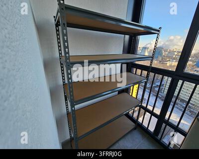 Ein hohes Regal mit einer Holzplatte oben drauf. Das Regal ist leer. Der Blick vom Balkon zeigt eine Stadt mit Kraftwerk Stockfoto